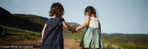Zwei Kinder laufen auf einem Weg in der Natur und halten sich dabei die Hand.