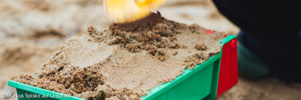 Ein Kind schaufelt gerade einen Spielzeuganhänger mit Sand voll