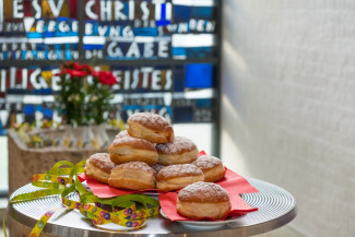 Ein Teller voll mit Krapfen zu sehen vor den Buntglasfenstern der Thomaskirche.