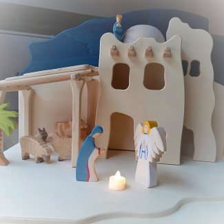 Die Krippe aus dem Fenster der Thomaskirche. Engel und Maria schauen auf ein Teelicht. Im Hintergrund zu sehen sind ein Haus und ein Stall. 